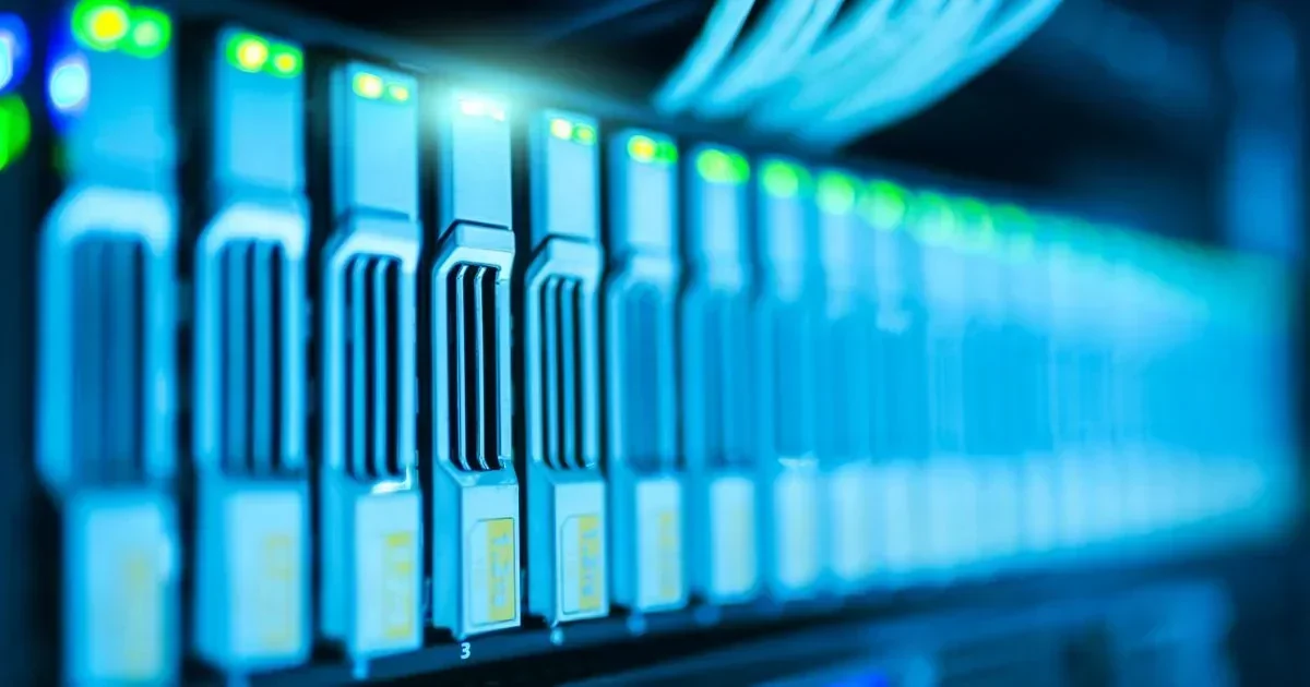 A close-up of illuminated blue server drives in a data center rack with green indicator lights and blurred cabling above.