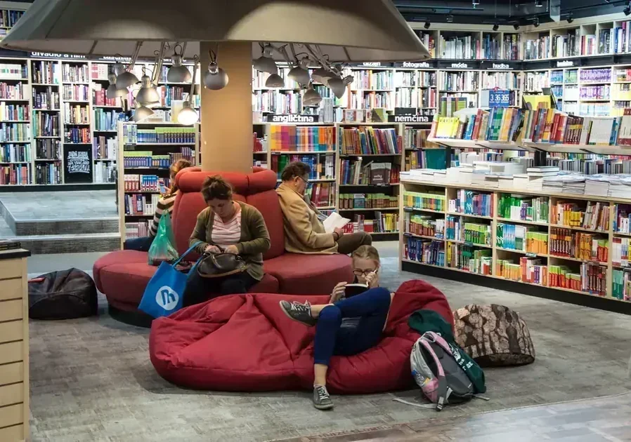 People reading on red beanbag chairs beneath a large lamp in a bookstore with multilingual shelves.