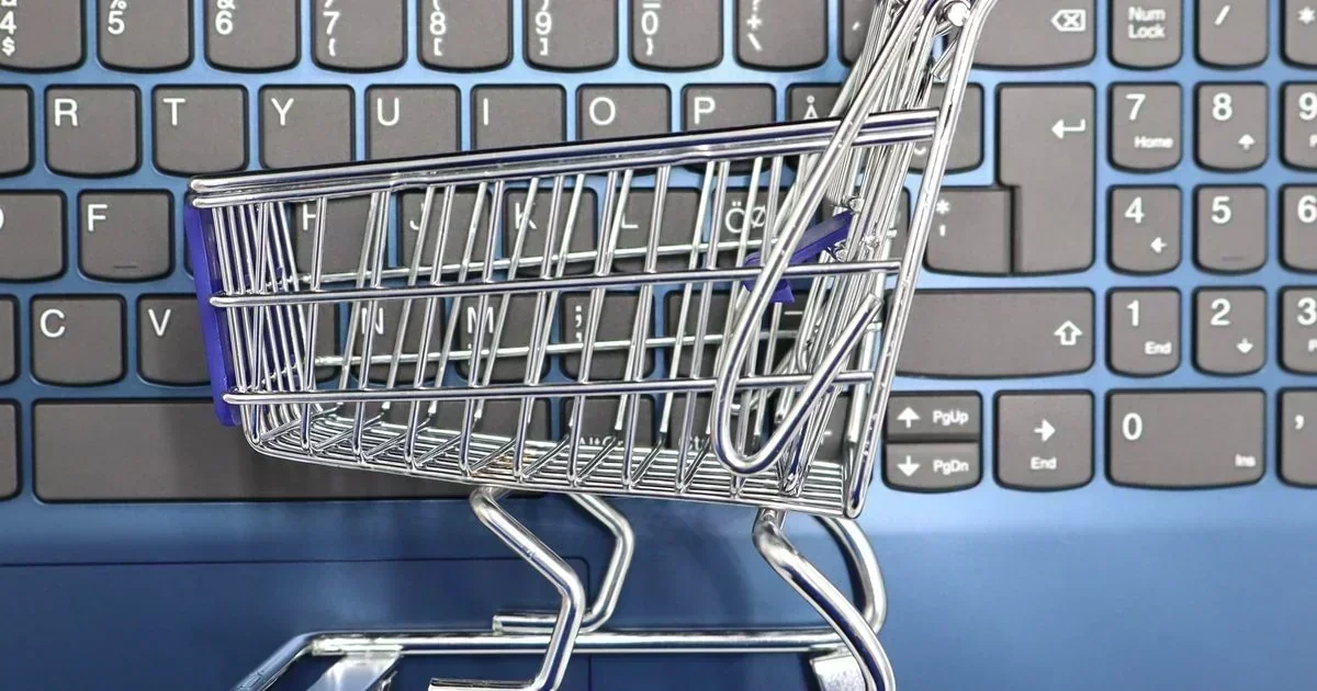 A miniature metal shopping cart rests on a blue computer keyboard, symbolizing online retail.