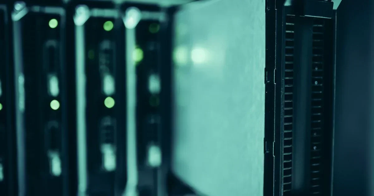 Rows of dark server racks with glowing green indicator lights line a data center aisle, with a blurred foreground rack on the right.
