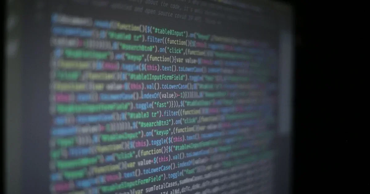 A close-up of a dark monitor showing colorful jQuery JavaScript code with functions for table filtering and click events.
