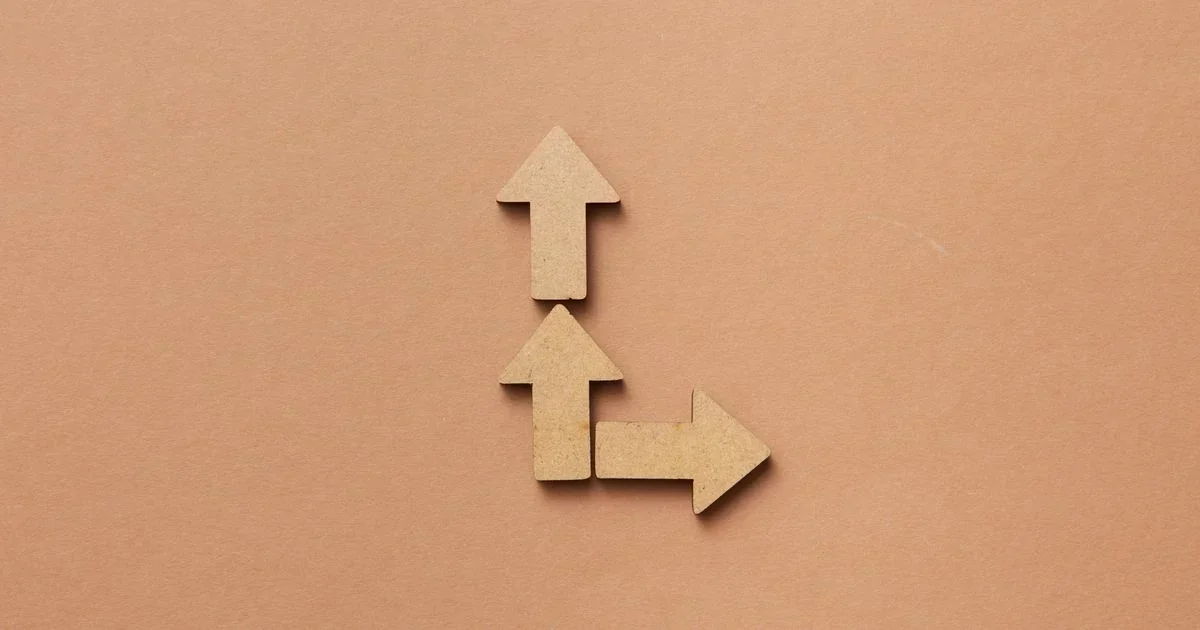 Three wooden arrows on a tan background, two pointing up and one pointing right, forming a branching path.